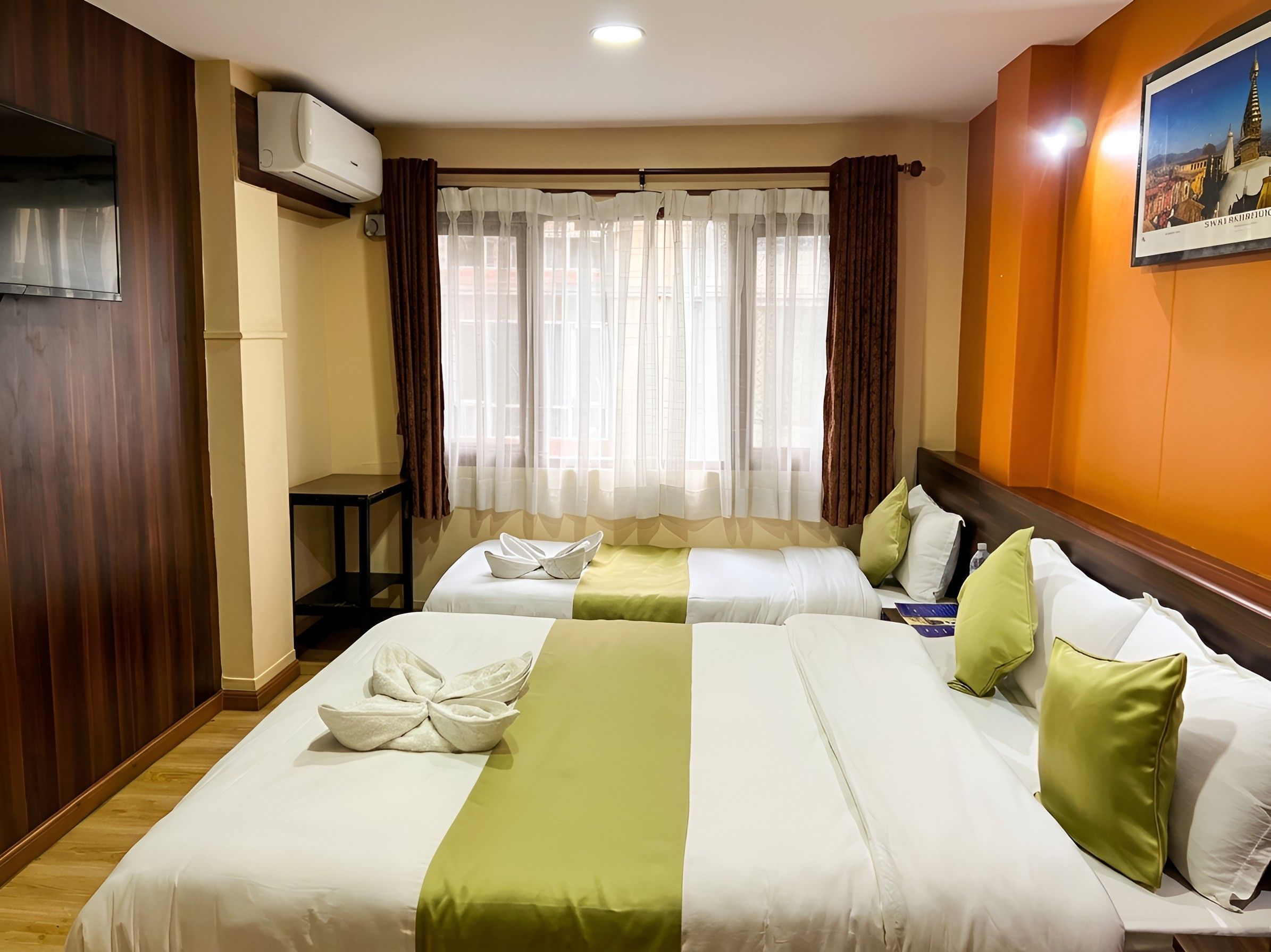 Habitación de hotel con dos camas, una ventana con cortinas translúcidas, un equipo de aire acondicionado y un cuadro en la pared.