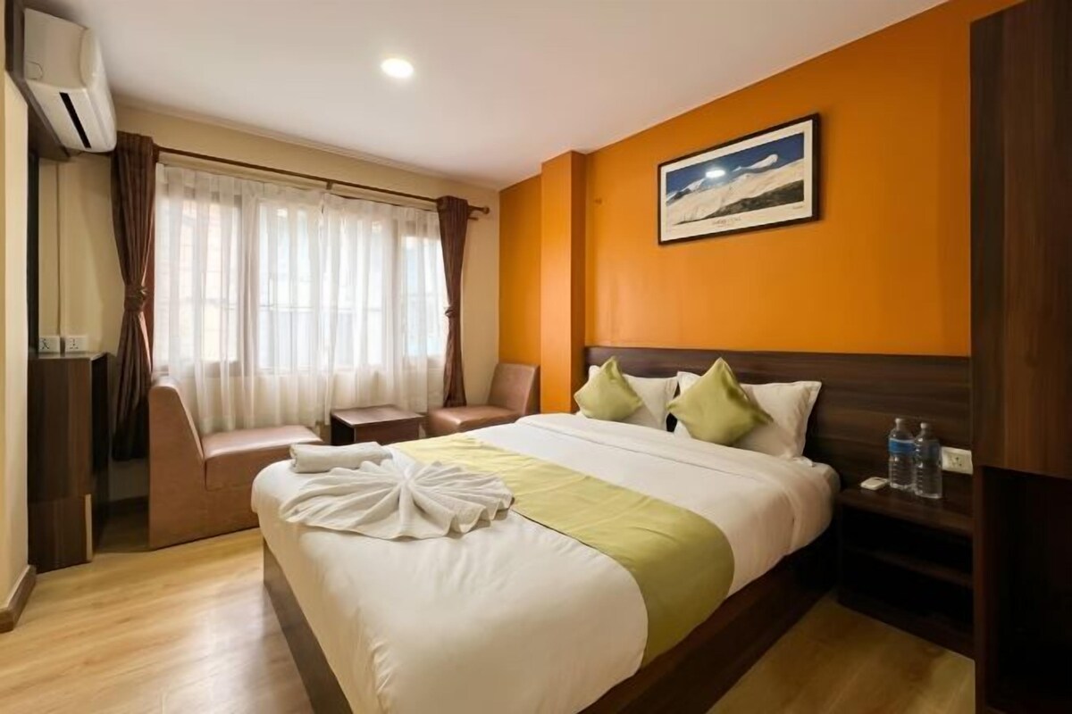 A hotel room with a bed, a chair, a nightstand, and a window with curtains.