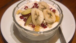 A bowl of yogurt with sliced bananas and pomegranate seeds on a white plate. - Holiday Hostel (Kathmandu)