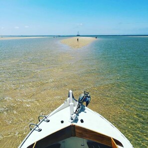 A boat on clear shallow water with a sandy beach and a distant sailboat. - La Cabane N°20, Plage à Pieds (Arès)