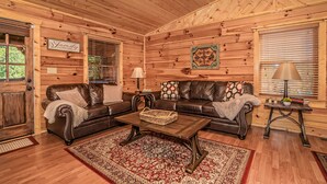 A wooden cabin interior with two leather sofas, a coffee table, and a patterned rug. - Get Hip ~ Close 2 Attractions - Hot tub - Firepit - King Suite - Flat Drive (Sevierville)