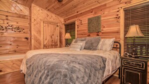 A wooden cabin bedroom with a bed, a nightstand, and a wall-mounted lamp. - Get Hip ~ Close 2 Attractions - Hot tub - Firepit - King Suite - Flat Drive (Sevierville)