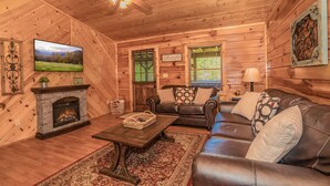 A cozy log cabin interior with a fireplace, leather sofa, and a television displaying a scenic landscape. - Get Hip ~ Close 2 Attractions - Hot tub - Firepit - King Suite - Flat Drive (Sevierville)