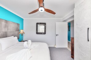 A hotel room with a bed, a ceiling fan, a nightstand, a lamp, a door, and a wall-mounted mirror. - Beachfront couples paradise overlooking Robben Island and Atlantic ocean. (Cape Town)