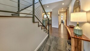 Una escalera moderna con barandas de metal, una consola de madera con una lámpara y un pasillo que conduce a una zona de cocina.