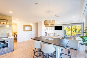 A modern kitchen with a central island, bar stools, and a dining area with a sofa and TV. - Beautiful new Peaks Penthouse- Ski-in & Ski-out with Amazing Views (Mountain Village)