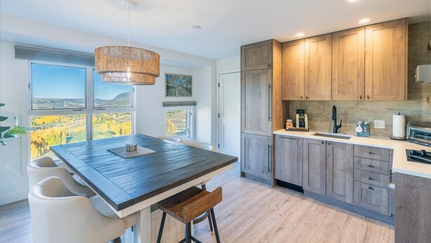 Eine moderne Küche mit Holzausstattung, einer großen Insel mit Sitzgelegenheit und Blick ins Freie durch große Fenster.
