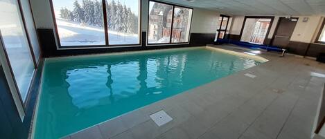 Una piscina interior con vistas claras a un paisaje nevado a través de amplios ventanales.
