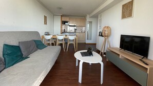 Un ambiente compatto con divano, tavolo da pranzo, sedie, televisore e angolo cottura.