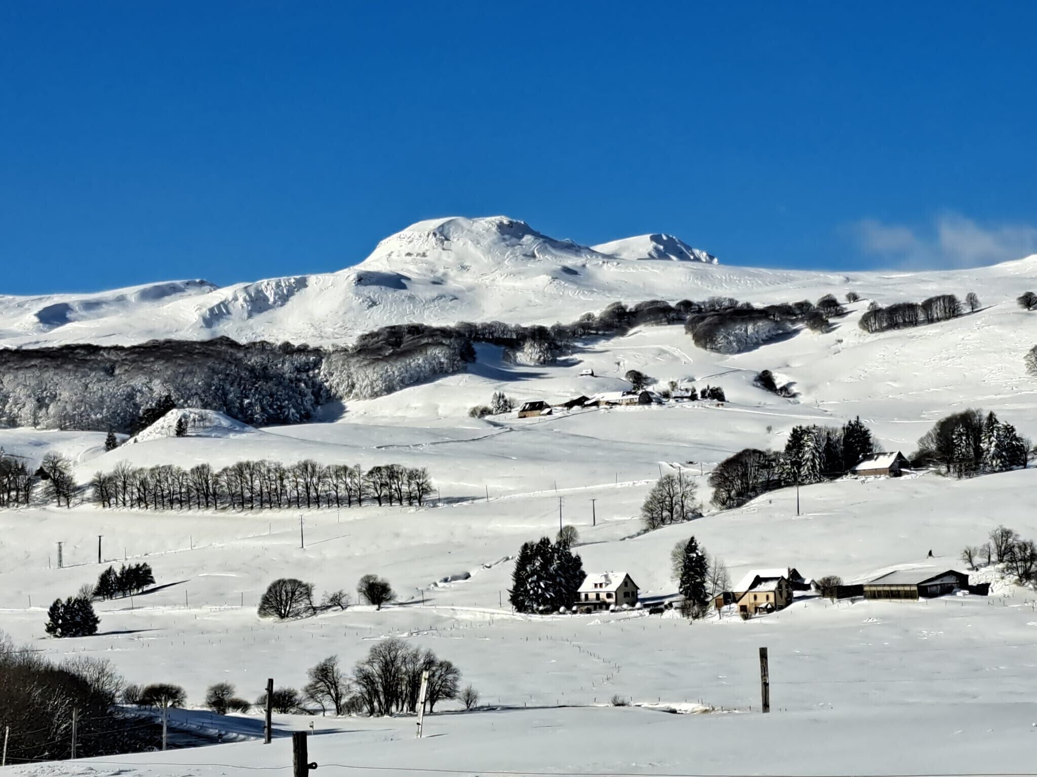 Un paisaje nevado con una montaña destacada, árboles dispersos y varios edificios.