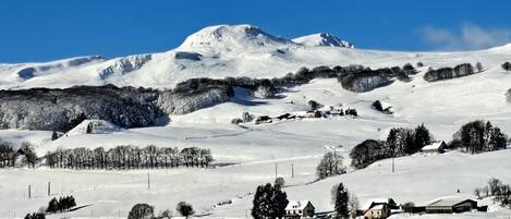 Un paisaje nevado con una montaña destacada, árboles dispersos y varios edificios.