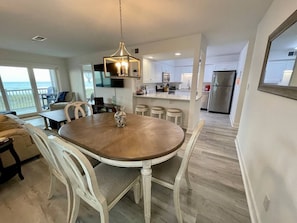A dining area with a round table and chairs, a hanging light fixture, and a view to the kitchen and balcony.