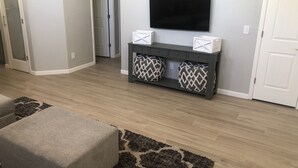A living room with a flat-screen TV mounted on the wall, a dark console table with decorative pillows, and a grey ottoman. - Beautiful, newly renovated Tucson Eastside home  (Tucson)