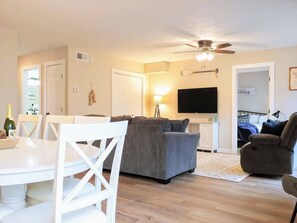 A living room with a grey sofa, white chairs, a TV, and a ceiling fan. - Water's Edge Retreat - Sleep 18, Two homes in one! (Branson)