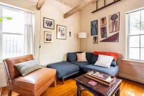 A living room with a brown leather sofa, a blue sectional sofa, and a wooden coffee table. There are framed pictures on the wall and a lamp on a side table. - The Railway Bridge Cottage (Catskill)
