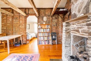 A cozy room with exposed brick walls, a fireplace, a wooden table, and a bookshelf. - The Railway Bridge Cottage (Catskill)