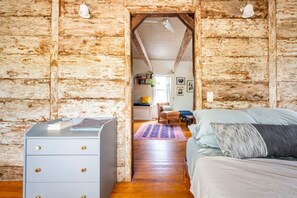 A rustic wooden room with a bed, a dresser, and a hallway leading to another room. - The Railway Bridge Cottage (Catskill)