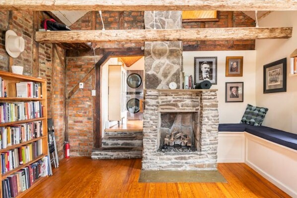A cozy room with a stone fireplace, wooden bookshelves, and a staircase leading to an upper level. - The Railway Bridge Cottage (Catskill)