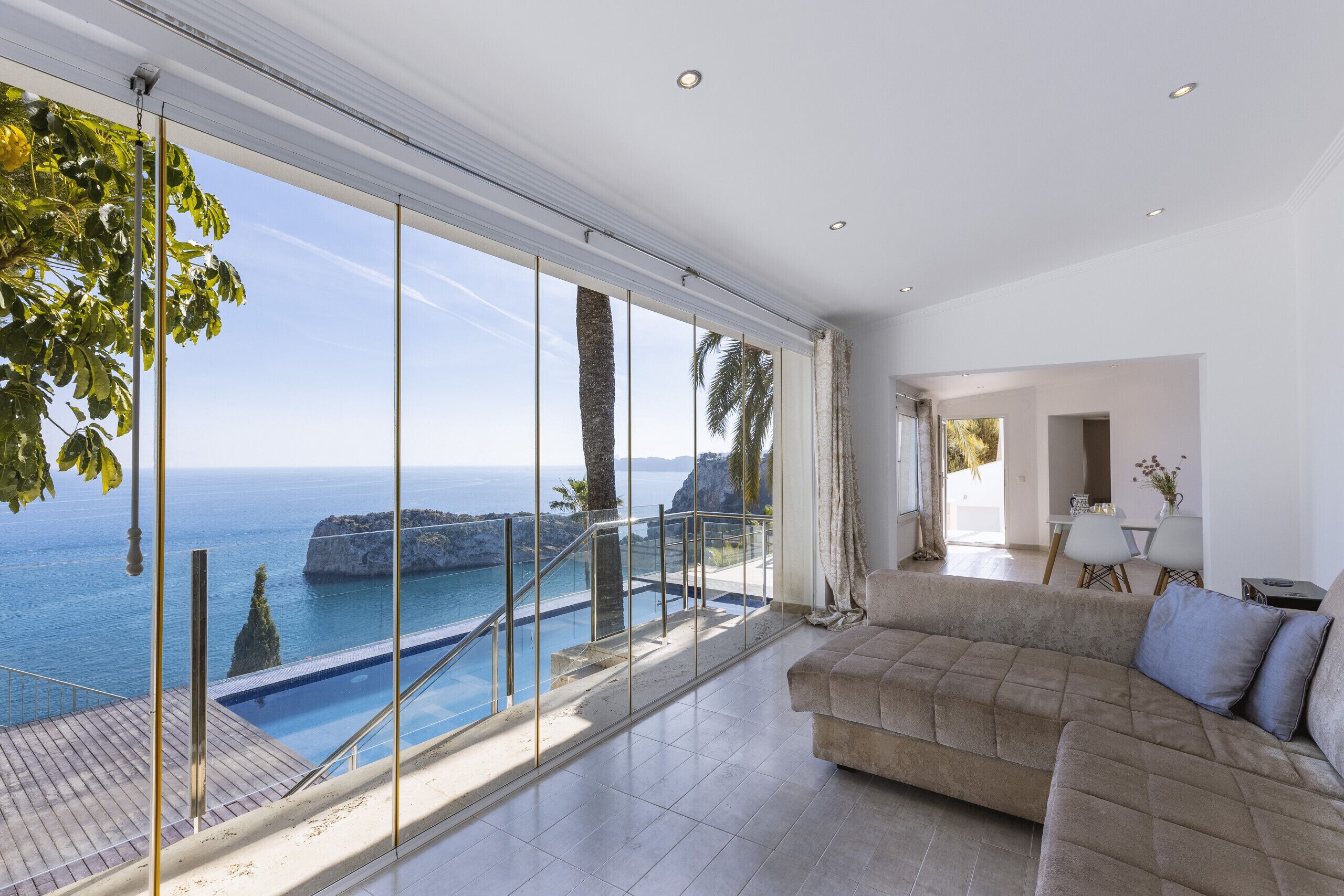 A spacious living room with a large window overlooking a pool and the sea.