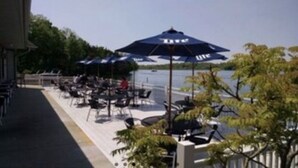 Zona all'aperto con tavoli e sedie, ombrelloni e vista sull'acqua.