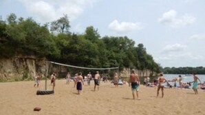 Una partita di beach volley su una spiaggia sabbiosa, con alberi sullo sfondo.