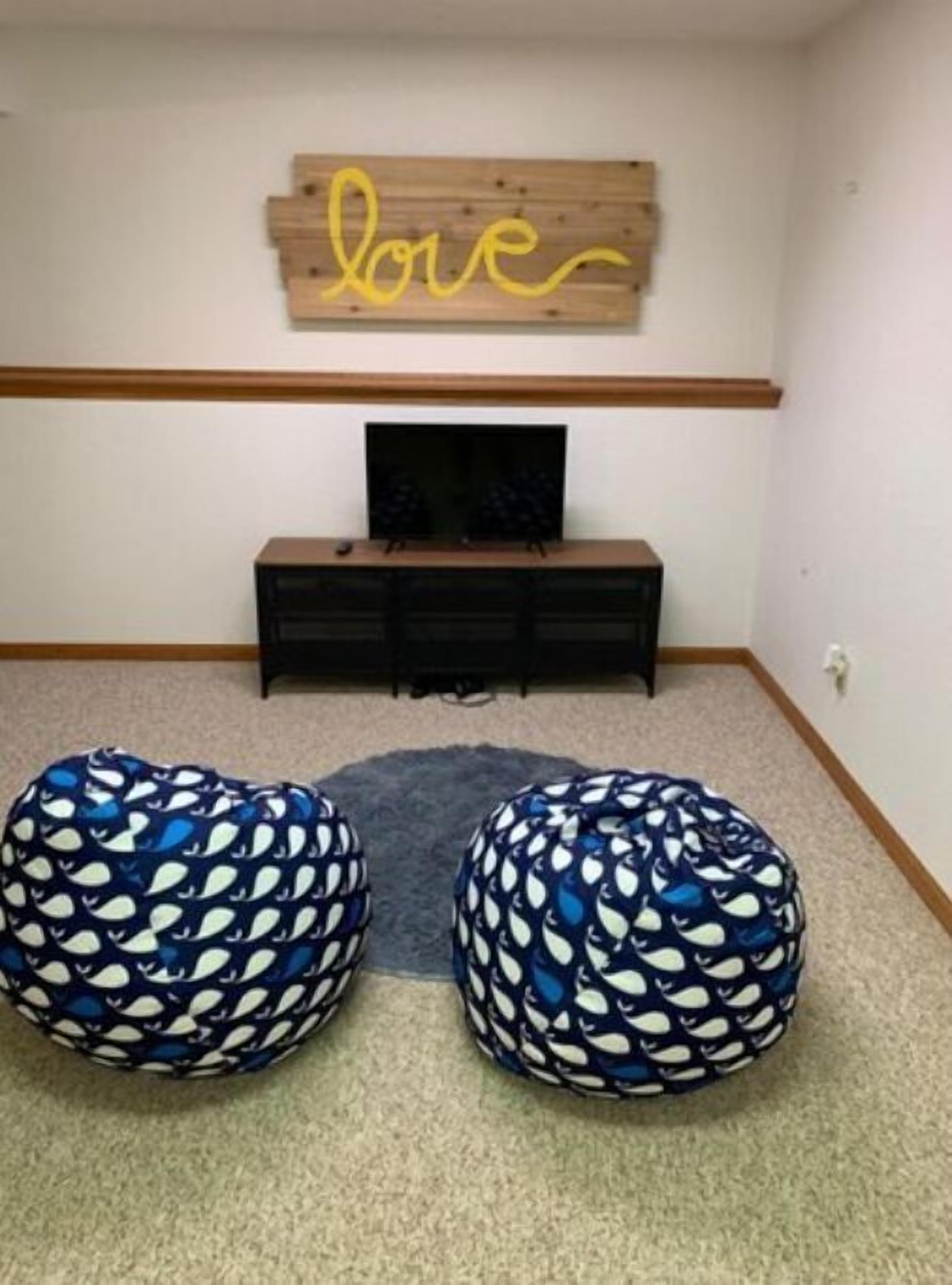 Een kamer met houten wanddecoratie met de tekst 'love', een televisie op een zwarte standaard en twee gestreepte zitzakken.