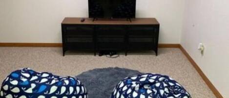 Een kamer met houten wanddecoratie met de tekst 'love', een televisie op een zwarte standaard en twee gestreepte zitzakken.