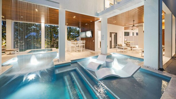 A modern indoor pool area with multiple seating areas and a television screen. - #1 Rooftop Deck w/ Gulf Views - Steps to Beach (Siesta Key)