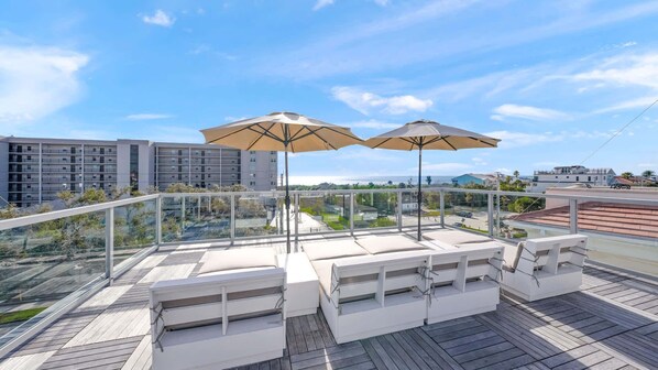 A rooftop terrace with outdoor seating, two large umbrellas, and a view of the cityscape.