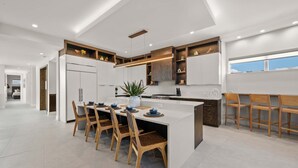 A modern kitchen with a central island, wooden chairs, and built-in cabinetry. - #1 Rooftop Deck w/ Gulf Views - Steps to Beach (Siesta Key)