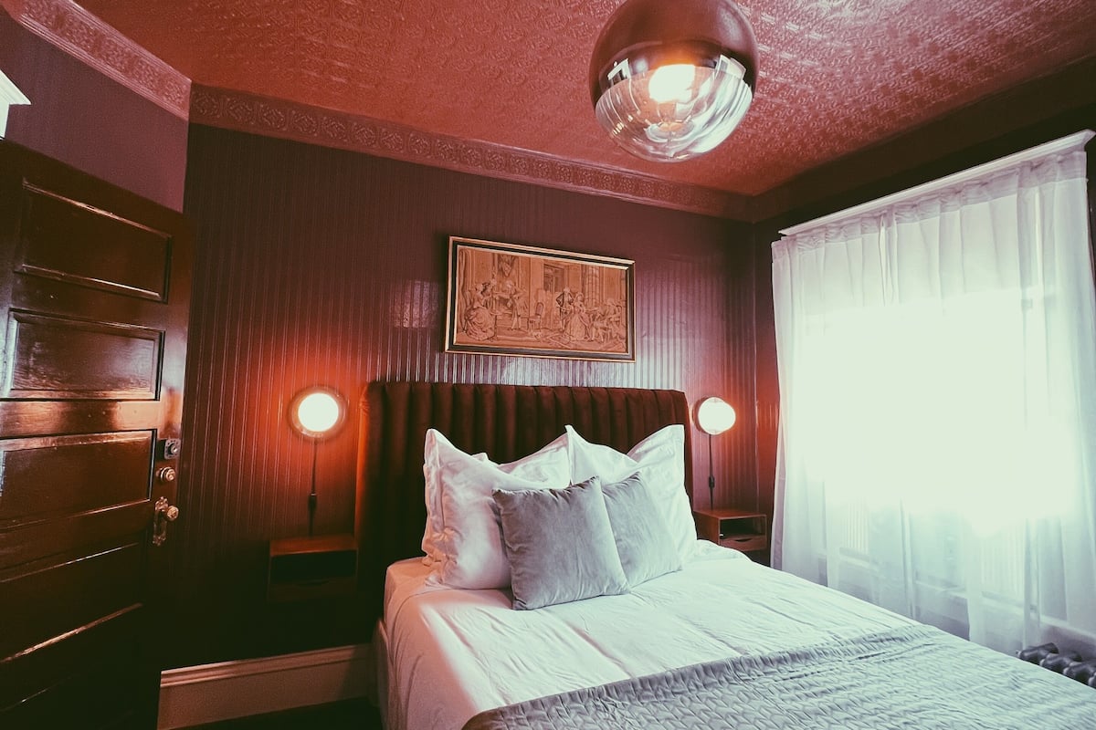 A hotel room with a large bed, a ceiling light, a framed picture on the wall, and a window with curtains.