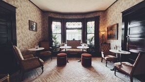 A room with patterned wallpaper, a chandelier, and multiple seating areas including armchairs and ottomans. - Marianna Stoltz House (Spokane)