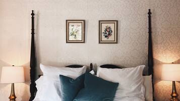 Ein ordentlich bezogenes Bett mit weißen und türkisfarbenen Kissen, begleitet von zwei an der Wand befestigten Bilderrahmen und Nachttischlampen auf beiden Seiten.