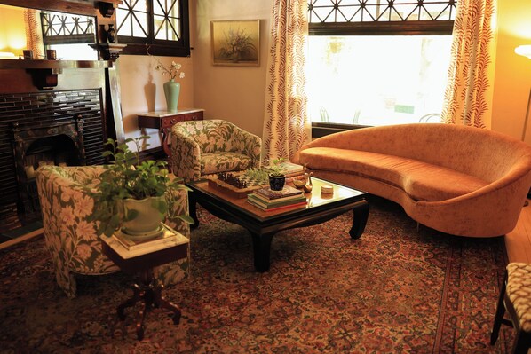 Una sala de estar acogedora con chimenea, un sillón estampado, sofá y una mesa de centro con libros y un florero.