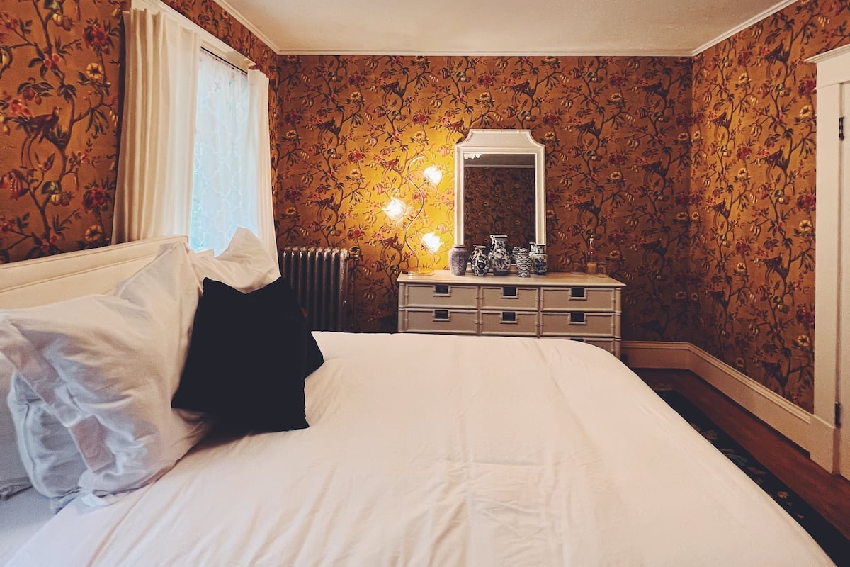 A bedroom with a bed, a dresser, a mirror, and a chandelier.