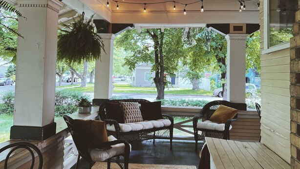 A covered patio area with string lights, seating, and a view of the outdoors. - Marianna Stoltz House (Spokane)