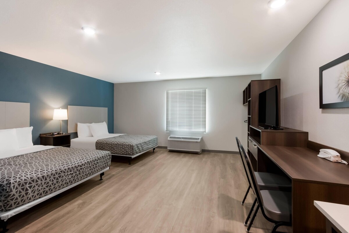 A hotel room with two beds, a desk, a chair, a TV, and a phone.