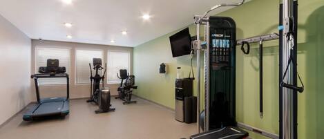 A gym with treadmills, elliptical machines, a bench, and a wall-mounted TV.