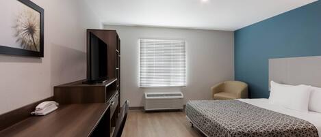 A hotel room with a bed, a desk, a chair, a television, and a window with blinds.