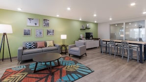 A modern living room with a sofa, coffee table, and chairs, a dining area with a table and chairs, and a kitchen area with a refrigerator and microwave. - Woodspring Suites Chandler Airport (Chandler)
