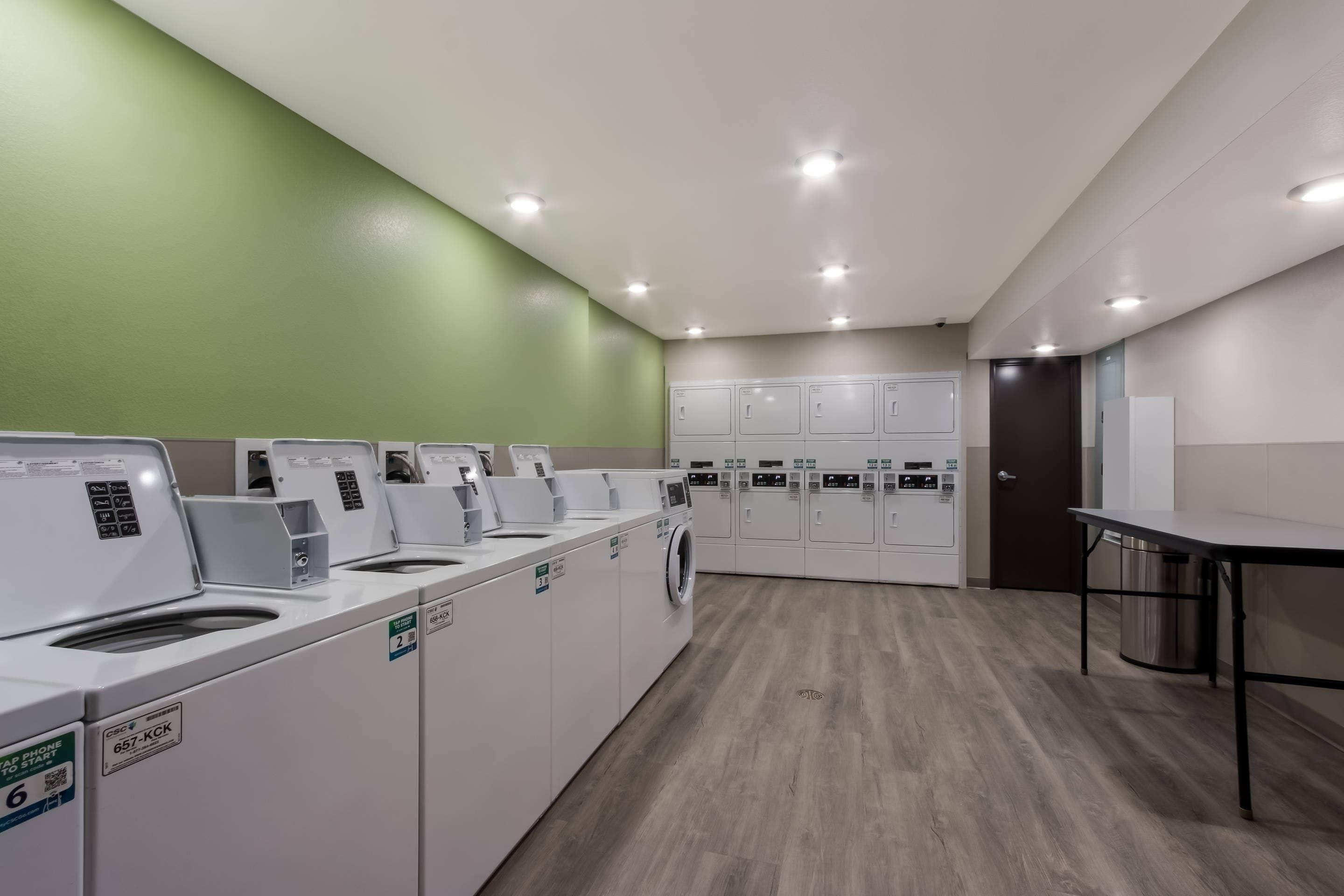 Une buanderie équipée de plusieurs machines à laver et de plusieurs sèche-linge, d’une table et d’un mur végétal.