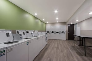 A laundry facility with multiple washing machines and dryers, a table, and a green wall.