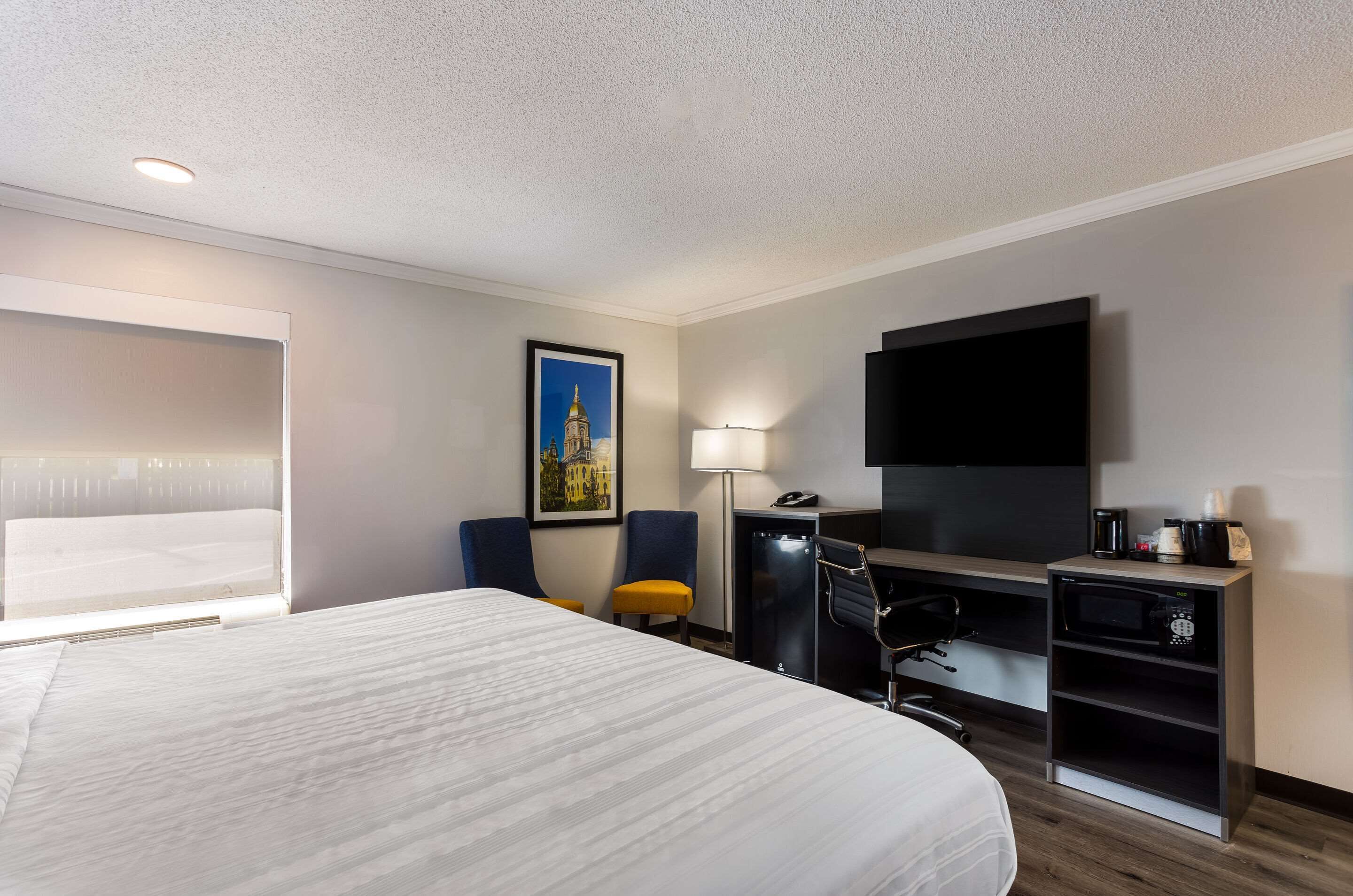 Habitación de hotel con una cama grande, un escritorio con computadora, una silla, televisor y cafetera.