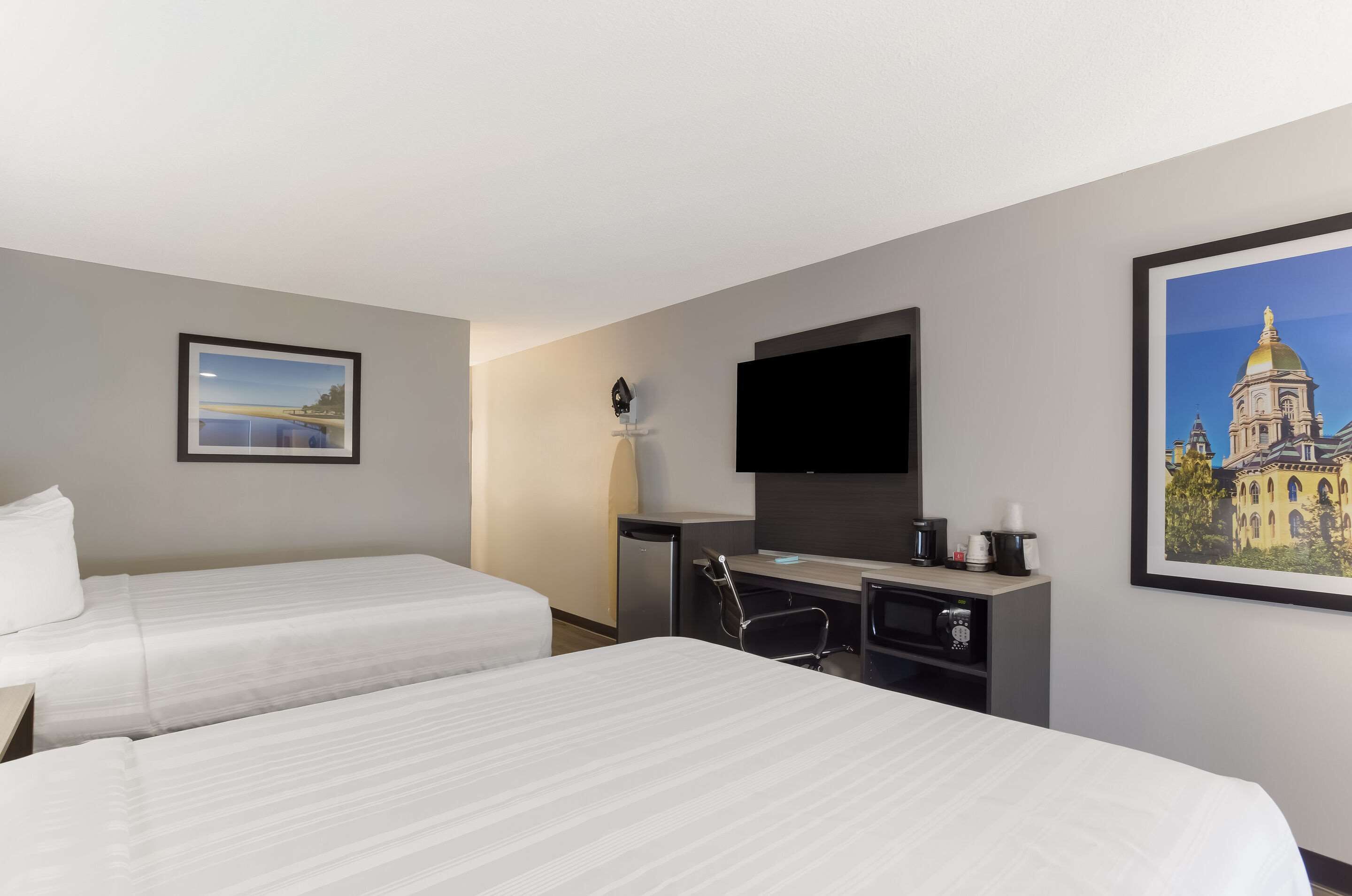 A hotel room with two beds, a desk with a chair, a flat-screen TV, and a coffee maker.