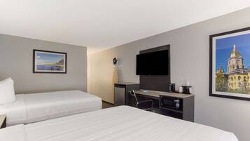 A hotel room with two beds, a desk with a chair, a flat-screen TV, and a coffee maker.