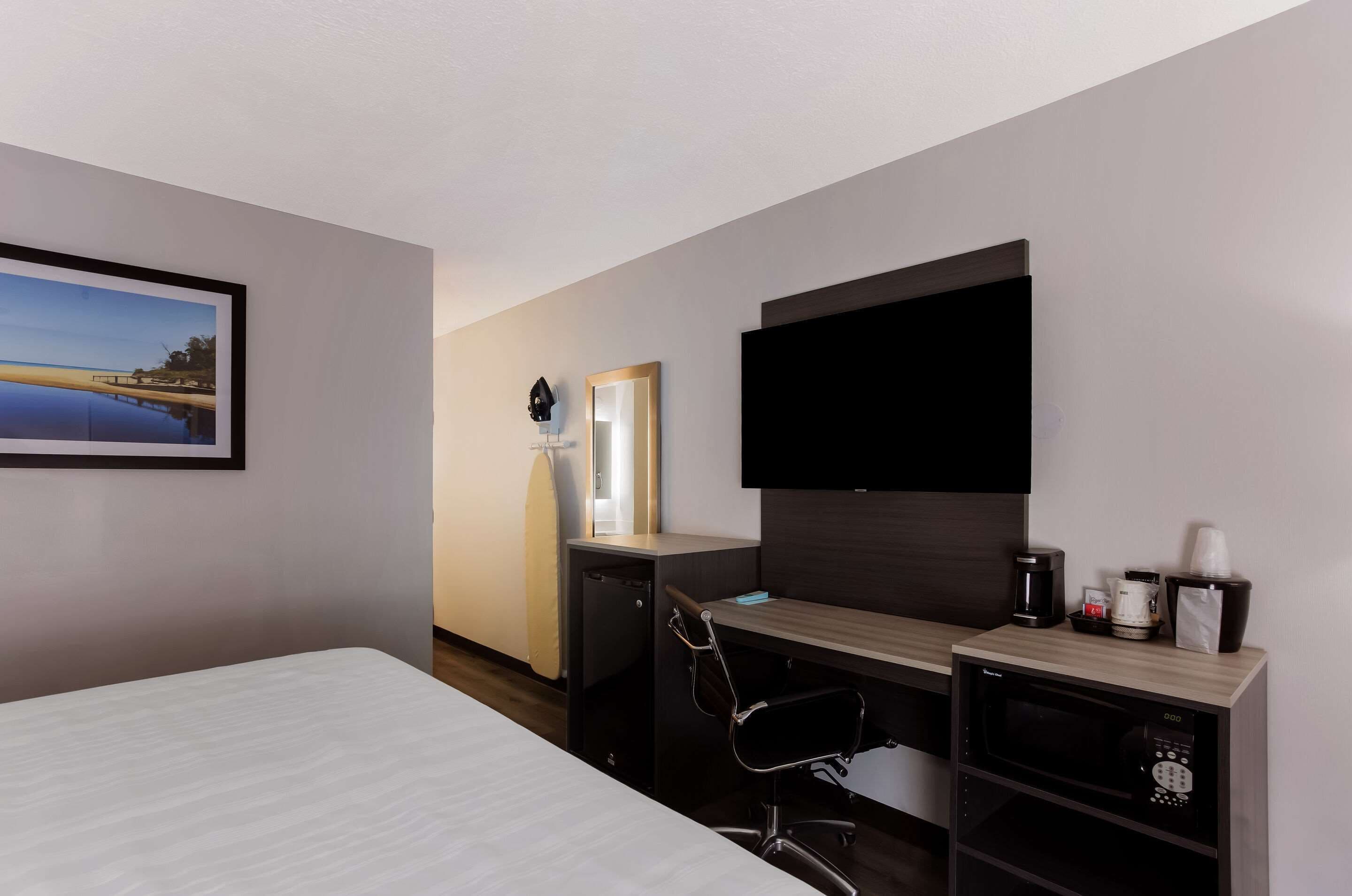 Habitación de hotel con cama, escritorio con computadora, televisor de pantalla plana, cafetera y microondas.