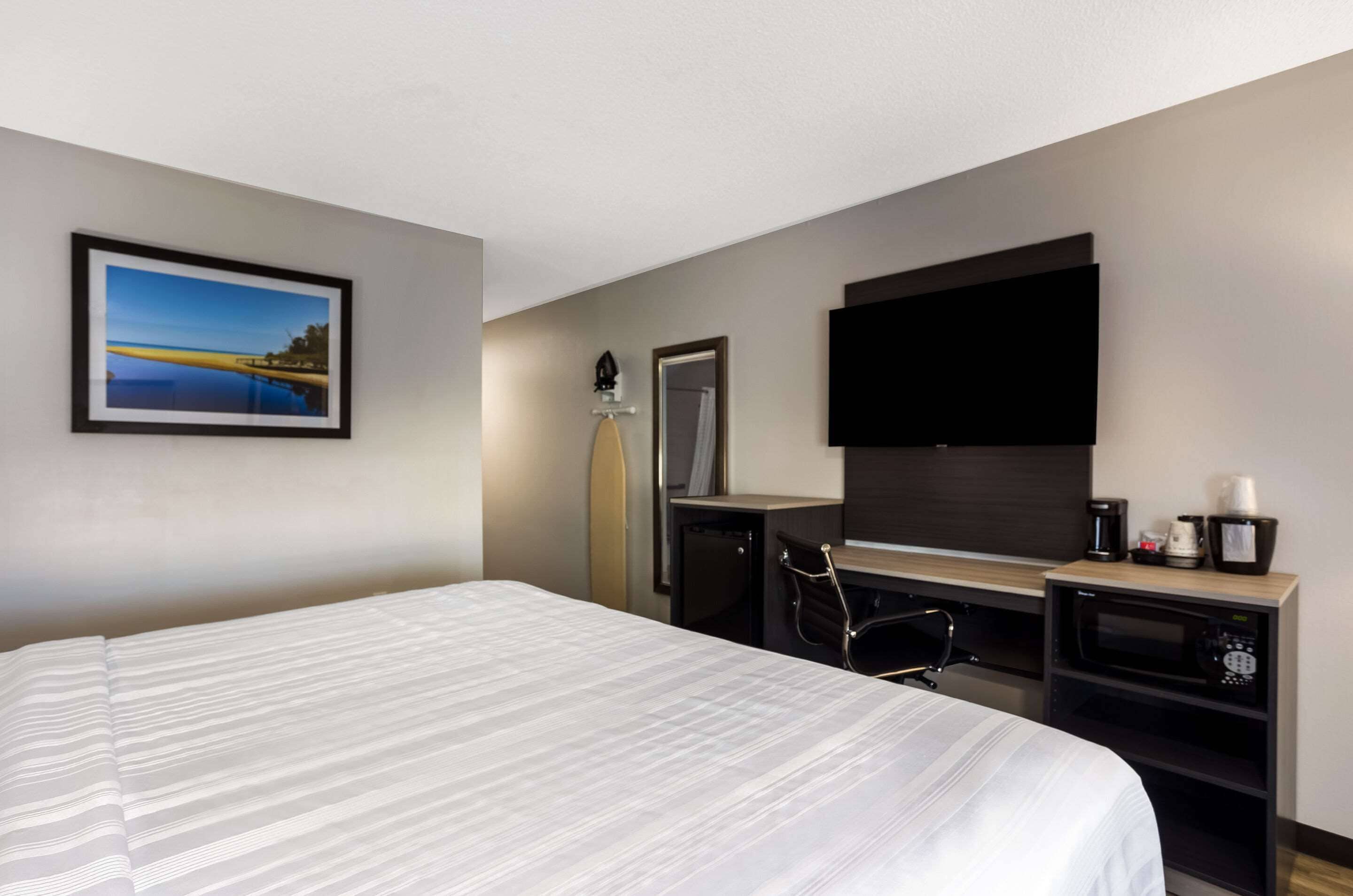 Ein Hotelzimmer mit einem großen Bett, einem Schreibtisch mit Fernseher, einer Kaffeemaschine und einem Wandbild mit Seeblick.