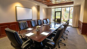 A conference room with a long table, black leather chairs, a projector screen, and large windows with a view of trees and hills.