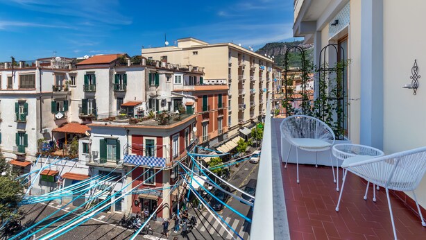 Un balcon avec des fauteuils en osier blanc, une vue sur la rue en contrebas et des immeubles dotés de balcons et de fenêtres.