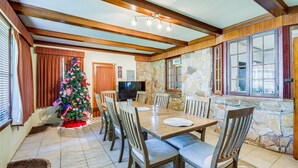 A dining area with a stone wall, wooden ceiling beams, a Christmas tree, and a television. - Cozy Jackson Vacation Rental < 1 Mi to University (Jackson)